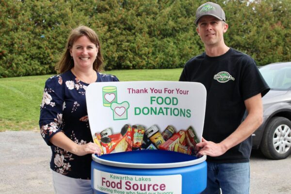 Two people smiling standing beside a food donation barrel