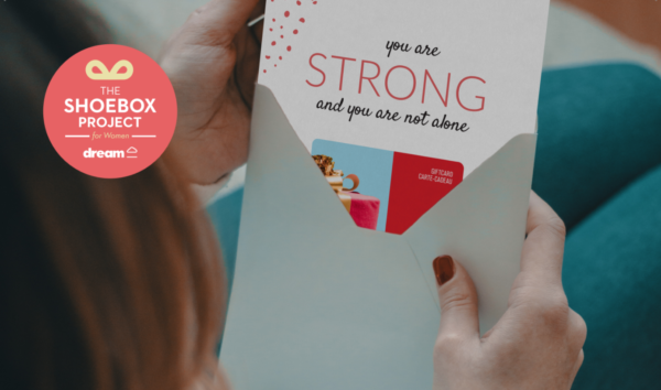 A woman opening an envelope which has a gift card enclosed. A message on the gift card reads "you are strong and you are not alone".