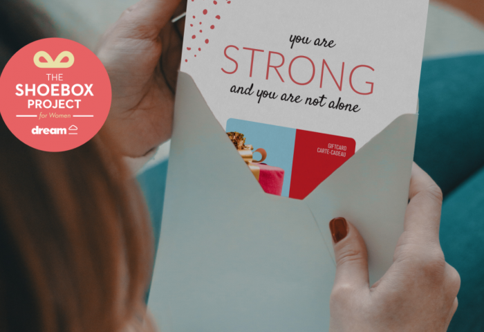 A woman opening an envelope which has a gift card enclosed. A message on the gift card reads "you are strong and you are not alone".