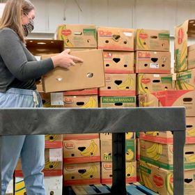 A woman stands in front of a stack of boxes, lifting one onto a cart